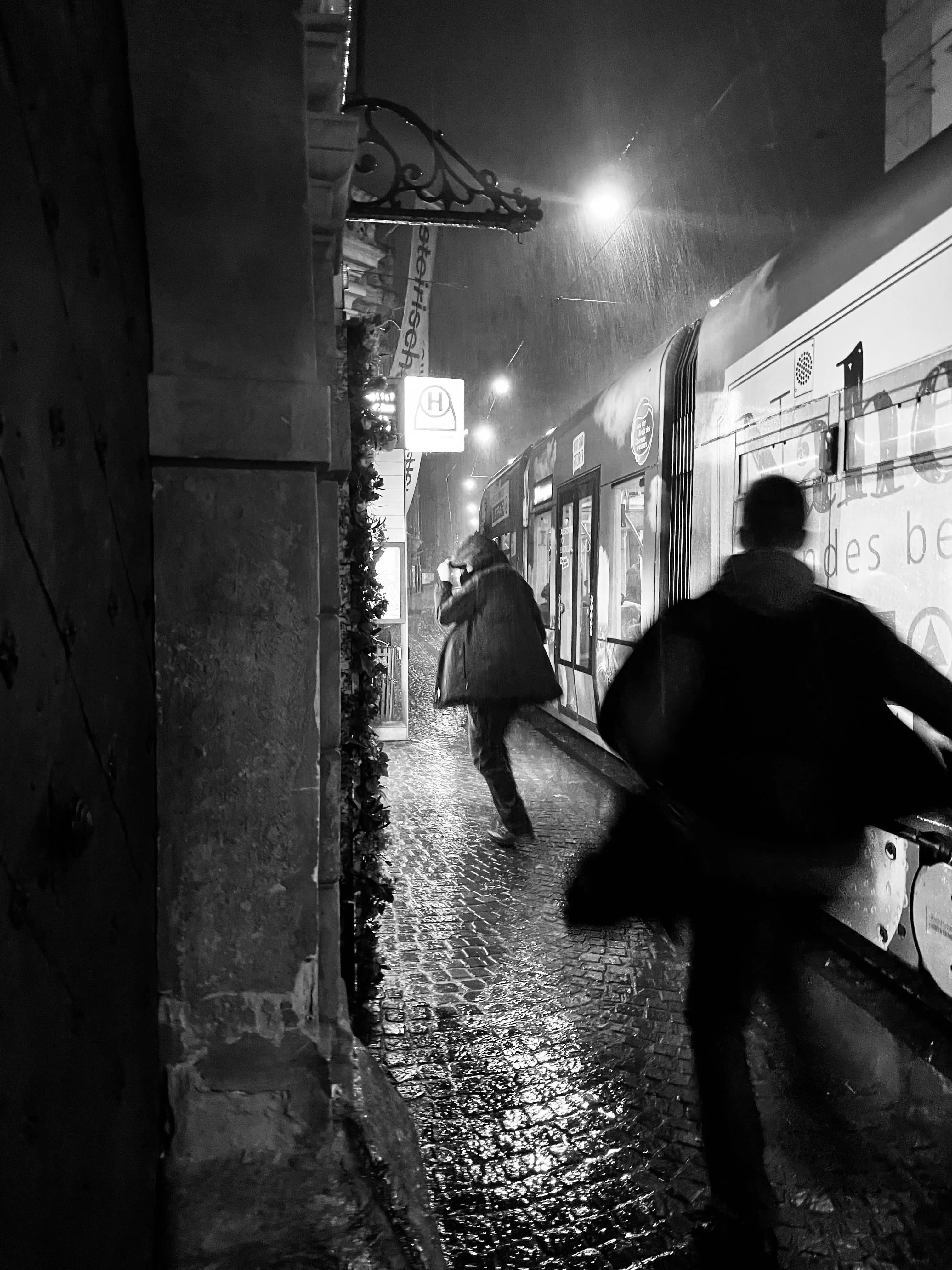 Pedestrians walking along a wet city street at night in black and white