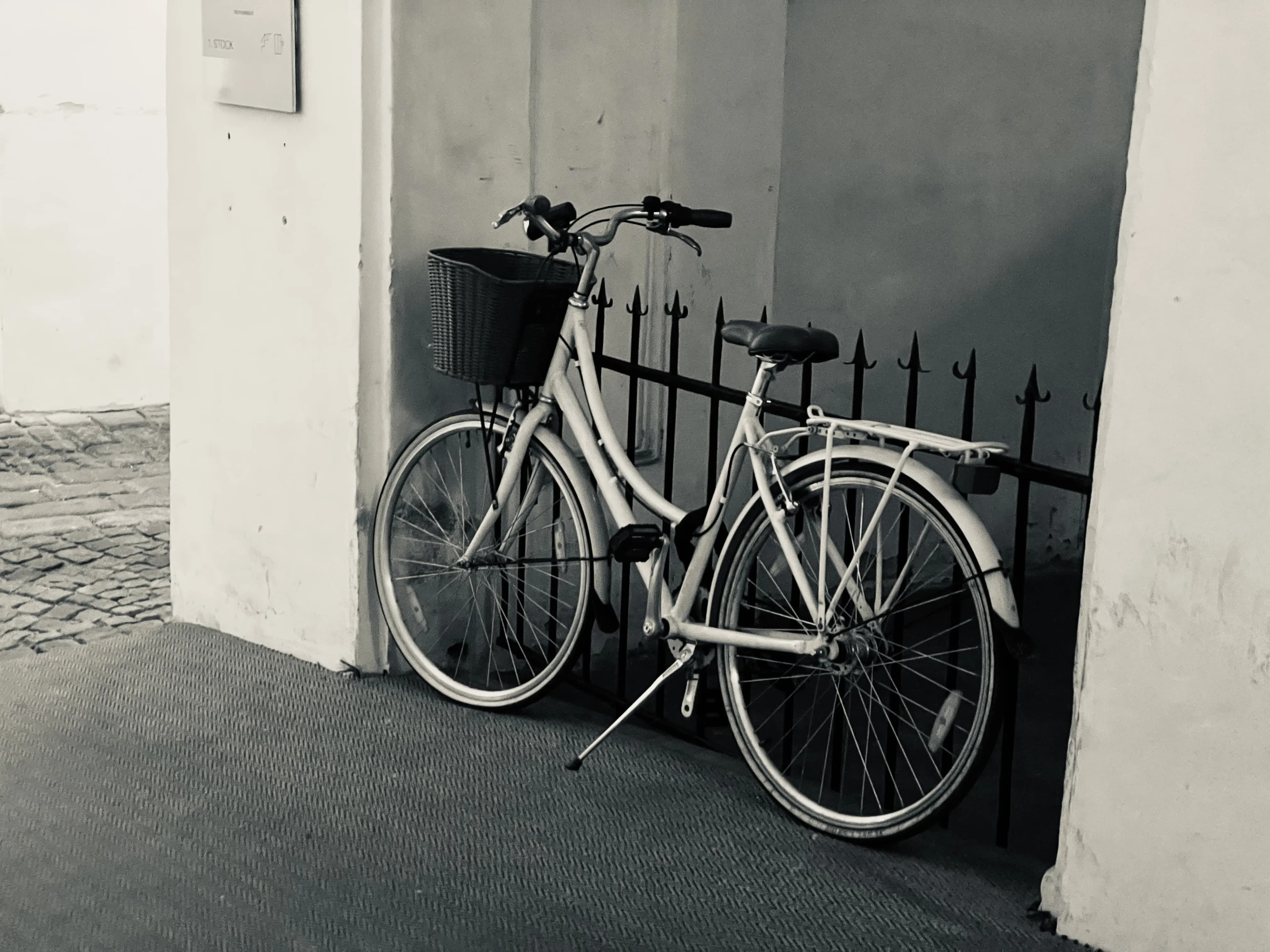 Two bicycles leaning against a railing beside a pale wall