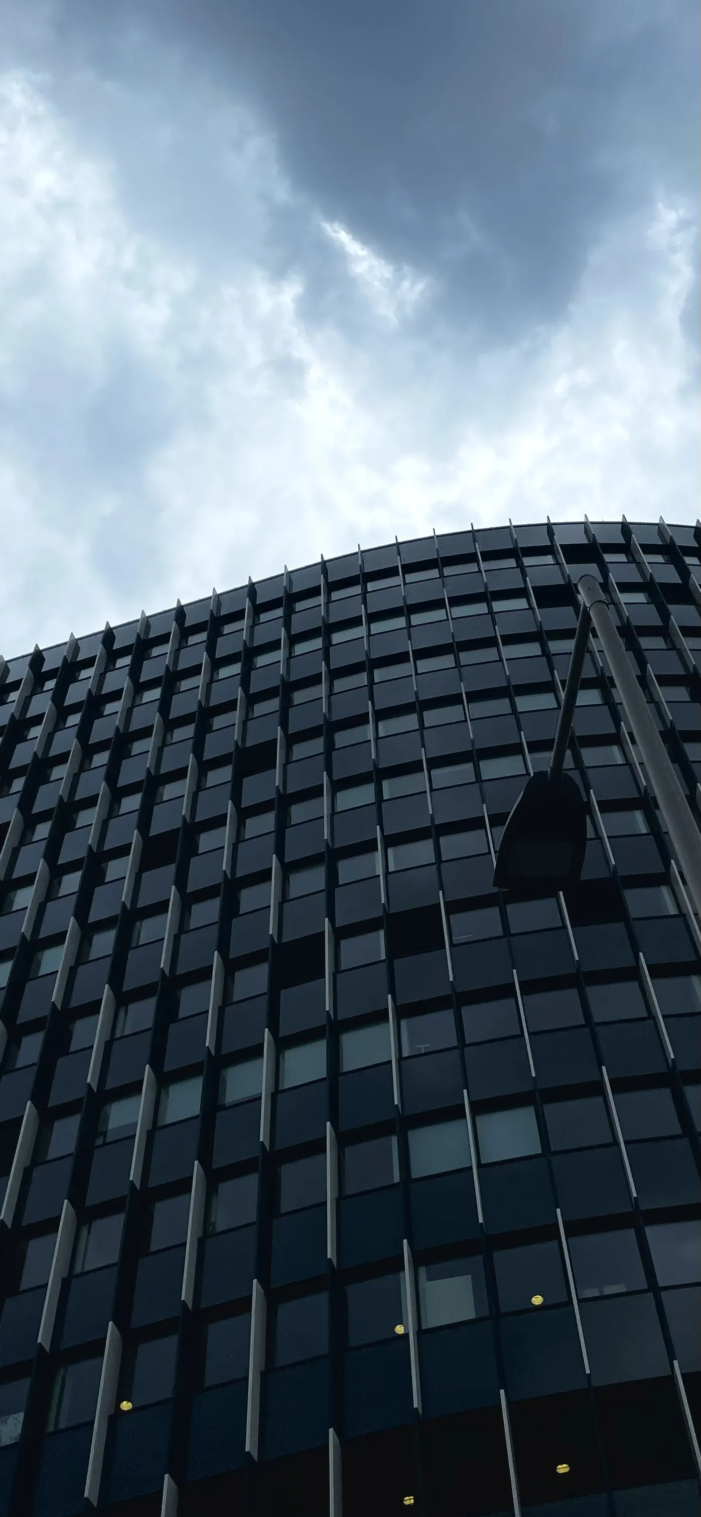 Narrow upward view of a glass building facade beneath dark clouds