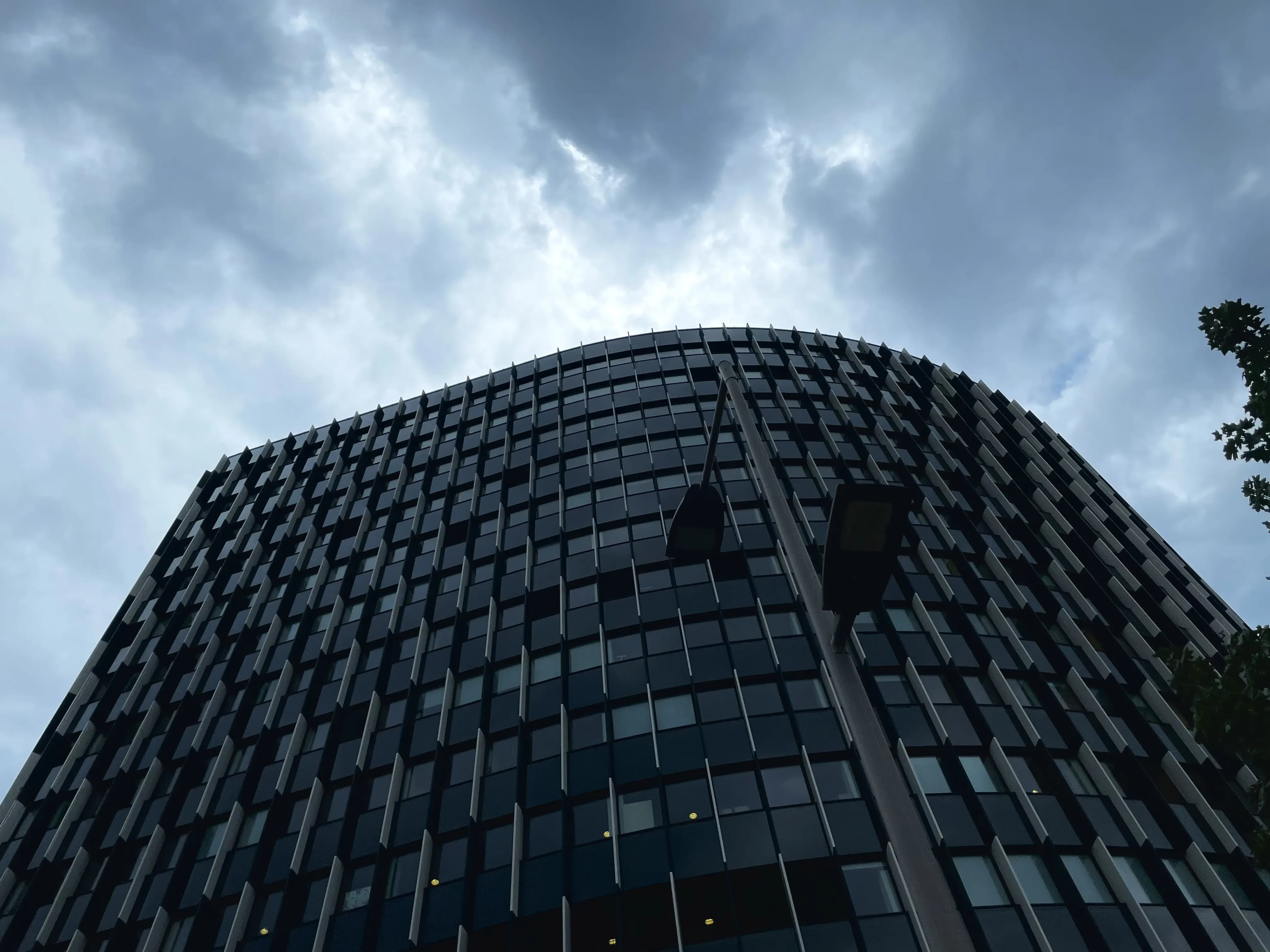 Curved glass office building viewed from below under storm clouds