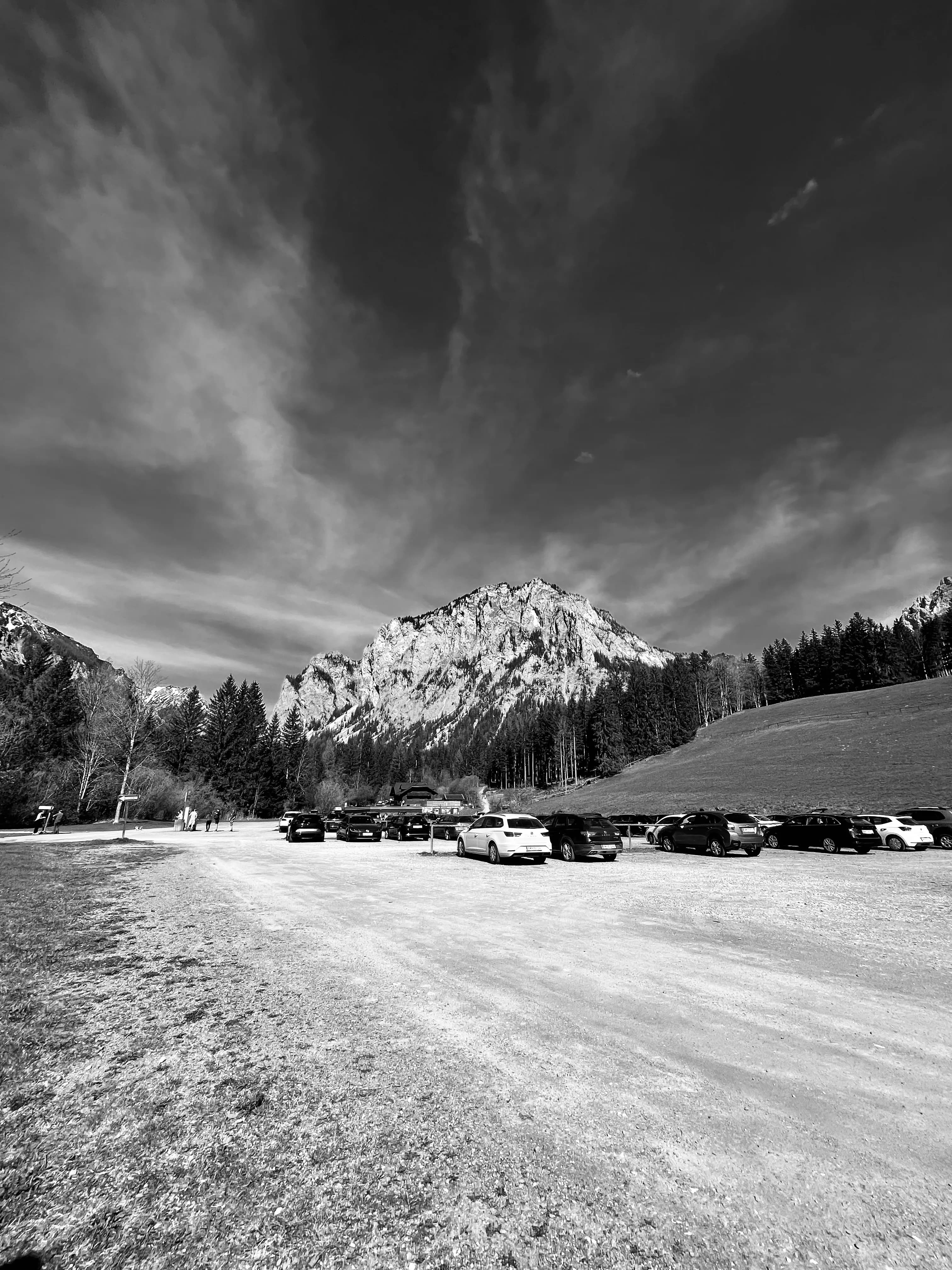 Black-and-white alpine field and scattered buildings below rugged peaks