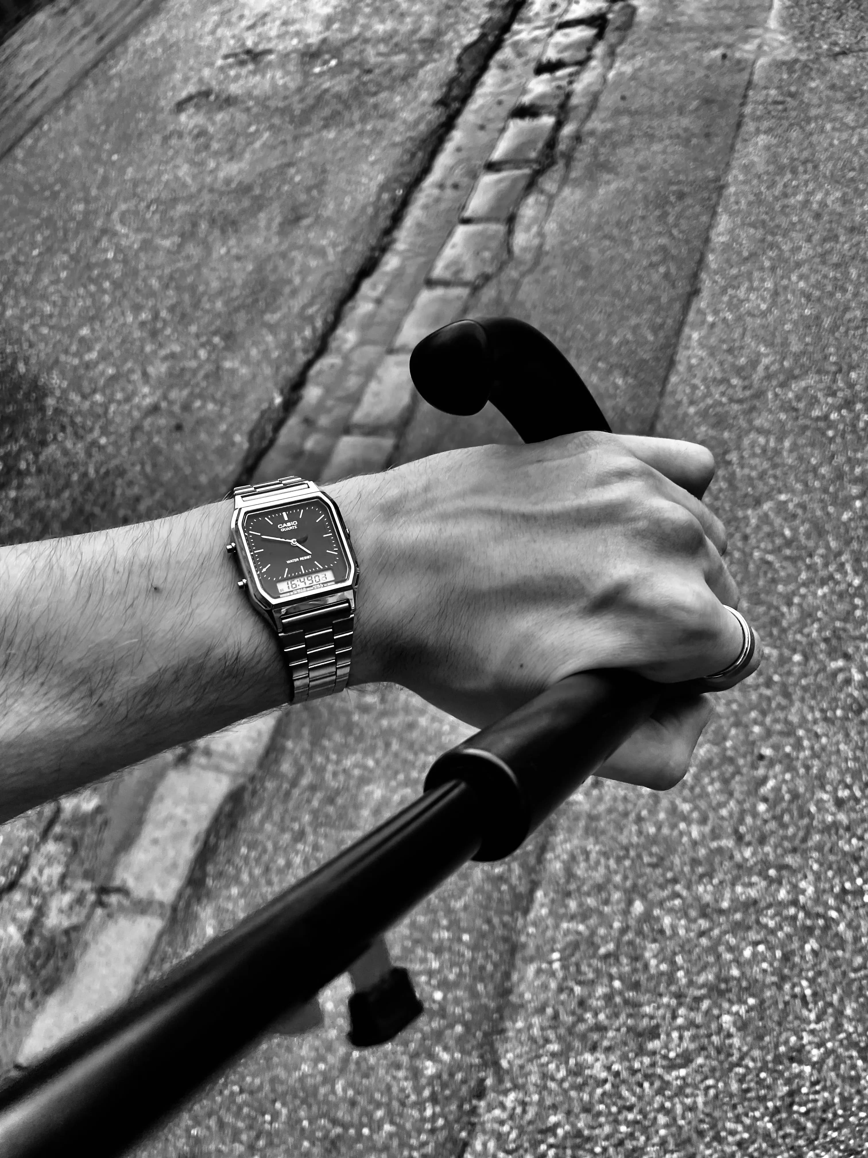 Black-and-white close-up of a watch-wearing hand on bicycle handlebars